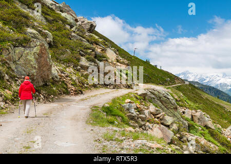 Une femme hauts randonnée randonneur sur un chemin de terre en été près de l'Ascher cabane dans la vallée de Paznaun en Autriche avec le Hoher Riffler en arrière-plan. Banque D'Images