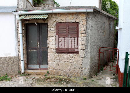 Pierre et petite maison en béton avec des portes en bois fissuré et fermé les stores avec nouvelle gouttière en métal blanc Banque D'Images