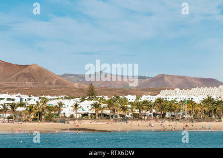 LANZAROTE - 14 janvier : les gens à la plage de Costa Teguise, Lanzarote, Espagne avec le village en arrière-plan le 14 janvier 2016. Banque D'Images