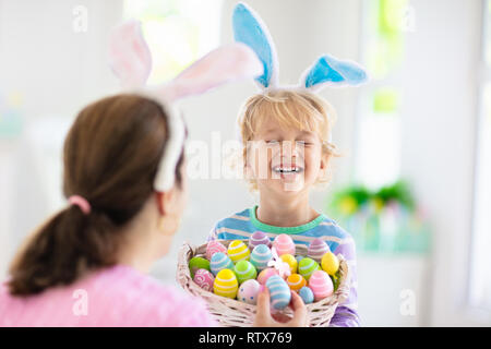 Mère et enfants la couleur des oeufs de Pâques. Petit garçon aux oreilles de lapin montrant maman oeufs bonbons colorés après chasse aux œufs de Pâques. Fête de famille et décor à la maison Banque D'Images