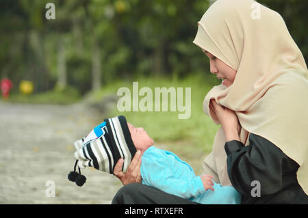 Heureux hijab musulman mère tenant un beau bébé pendant que son todler pleurer dans l'espace en plein air