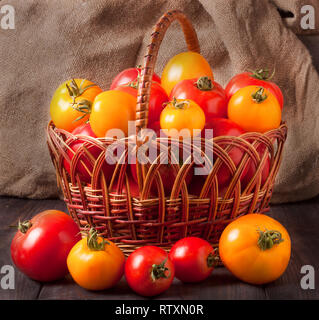 Les tomates rouges et jaunes dans un panier en osier sur la table en bois Banque D'Images