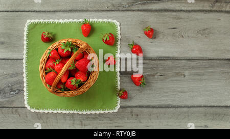 Vue sur table, panier de fraises, certains d'entre eux renversé sur une nappe verte en dessous. Banque D'Images