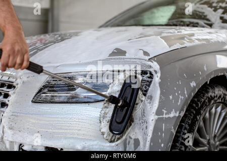 Lumière avant de silver car lavés dans le libre service carwash, man hand holding pinceau, nettoyage de la vitre avec du shampoing Banque D'Images