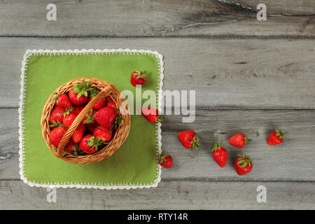 Photo de table, panier de fraises , certains d'entre eux renversé sur une nappe verte et grise bureau en bois. Banque D'Images