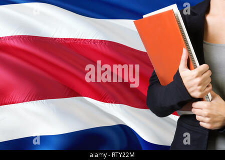 Concept L'apprentissage de la langue. Jeune femme debout avec le Costa Rica drapeau dans l'arrière-plan. Teacher holding books, couverture de livre blanc orange. Banque D'Images