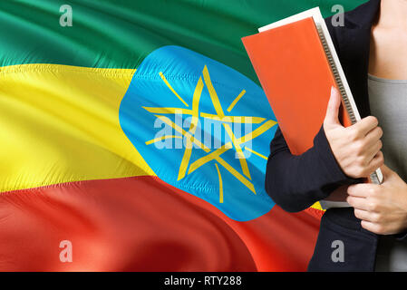 Concept d'apprentissage de la langue éthiopienne. Jeune femme debout avec le drapeau de l'Éthiopie à l'arrière-plan. Teacher holding books, couverture de livre blanc orange. Banque D'Images