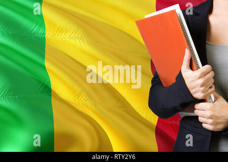 Concept d'apprentissage des langues maliennes. Jeune femme debout avec le Mali drapeau dans l'arrière-plan. Teacher holding books, couverture de livre blanc orange. Banque D'Images