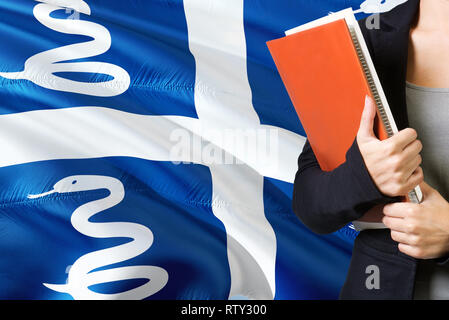 Concept L'apprentissage de la langue. Jeune femme debout avec le drapeau de la Martinique dans l'arrière-plan. Teacher holding books, couverture de livre blanc orange. Banque D'Images