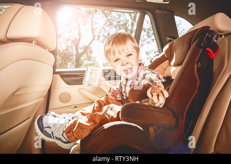 Adorable bébé garçon est rire, jouer avec de petites jumelles et tenant une pomme alors qu'il était assis dans le siège de la voiture de sécurité. Vue de côté Banque D'Images