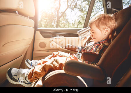 Adorable bébé garçon est rire, jouer avec de petites jumelles alors qu'il était assis dans le siège de la voiture de sécurité. Vue de côté Banque D'Images