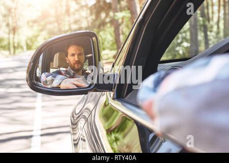 Jeune homme à la voiture pilote en vue de côté miroir, s'assurer que la ligne est libre avant de faire un tour. Bon voyage, voyage concept de conduite. Banque D'Images