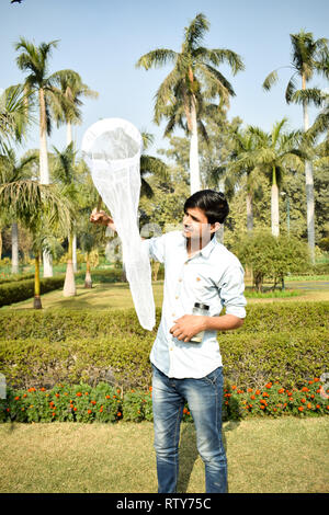 Jeune homme la collecte à l'aide d'un entomologiste Insectes Insectes net ou de la glisser pour sa collecte de spécimens d'insectes pendant un été lumineux Banque D'Images