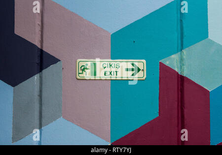 Enseigne de sortie vert en langue turque et en langue anglaise avec symbole de l'homme qui court à une porte. Sur la peinture murale géométrique. Banque D'Images