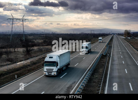 Caravane ou d'un convoi de camions camion blanc sur la route de pays sous un ciel dramatique Banque D'Images