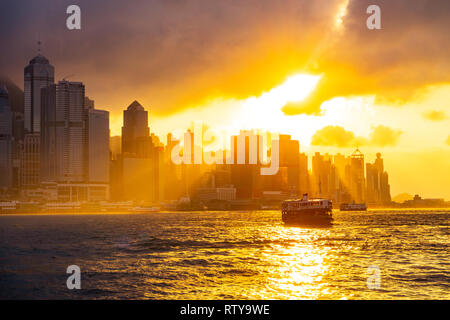 Silhouette de Star Ferry traversant le port de Victoria au coucher du soleil et la ligne d'horizon de Hong Kong, Chine Banque D'Images