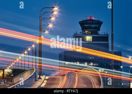 Les sentiers de la lumière de la voiture sur la route de l'aéroport contre une tour de contrôle de la circulation aérienne. Banque D'Images