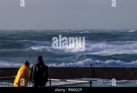 Sennen, Cornwall, UK. Le 3 mars 2019. Des coups de vent et des vagues hautes de 20 pieds lash le granite abruptes de Cornwall. Les cavaliers de l'audace de se faire prendre par des énormes vagues submergeant l'embarcadère. Crédit : Mike Newman/Alamy Live News. Banque D'Images