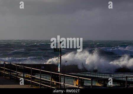 Sennen, Cornwall, UK. Le 3 mars 2019. Des coups de vent et des vagues hautes de 20 pieds lash le granite abruptes de Cornwall. Les cavaliers de l'audace de se faire prendre par des énormes vagues submergeant l'embarcadère. Crédit : Mike Newman/Alamy Live News. Banque D'Images