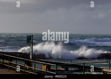 Sennen, Cornwall, UK. Le 3 mars 2019. Des coups de vent et des vagues hautes de 20 pieds lash le granite abruptes de Cornwall. Les cavaliers de l'audace de se faire prendre par des énormes vagues submergeant l'embarcadère. Crédit : Mike Newman/Alamy Live News. Banque D'Images