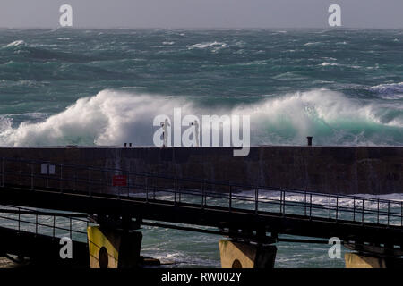 Sennen, Cornwall, UK. Le 3 mars 2019. Des coups de vent et des vagues hautes de 20 pieds lash le granite abruptes de Cornwall. Les cavaliers de l'audace de se faire prendre par des énormes vagues submergeant l'embarcadère. Crédit : Mike Newman/Alamy Live News. Banque D'Images