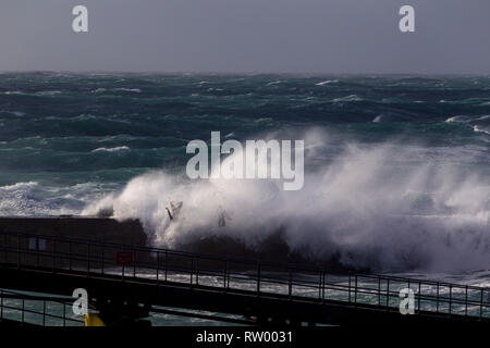 Sennen, Cornwall, UK. Le 3 mars 2019. Des coups de vent et des vagues hautes de 20 pieds lash le granite abruptes de Cornwall. Les cavaliers de l'audace de se faire prendre par des énormes vagues submergeant l'embarcadère. Crédit : Mike Newman/Alamy Live News. Banque D'Images