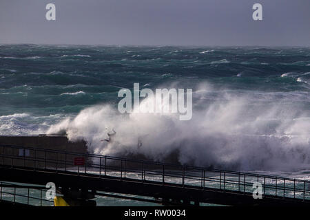 Sennen, Cornwall, UK. Le 3 mars 2019. Des coups de vent et des vagues hautes de 20 pieds lash le granite abruptes de Cornwall. Les cavaliers de l'audace de se faire prendre par des énormes vagues submergeant l'embarcadère. Crédit : Mike Newman/Alamy Live News. Banque D'Images