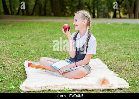 Happy smiling student avec apple en main. lycéenne assis sur une couverture dans un parc avec les manuels scolaires et à faire leurs devoirs Banque D'Images