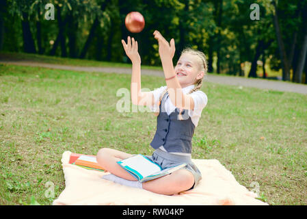 L'étudiant est souriant joyeusement et tient une pomme rouge au-dessus. lycéenne assis sur une couverture dans un parc avec des livres et à faire leurs devoirs Banque D'Images