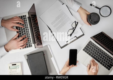 Vue de dessus d'entrepreneurs de la saisie sur des ordinateurs portables, holding smartphone et tasse de papier Banque D'Images