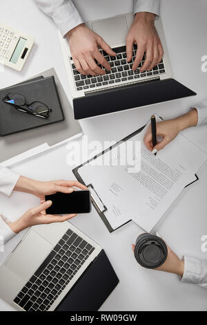 Vue de dessus d'entrepreneurs de la saisie sur ordinateur portable, holding smartphone et tasse de papier, document signature Banque D'Images