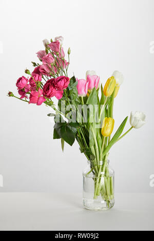 Roses roses fraîches et de tulipes jaunes dans un bocal en verre isolated on white Banque D'Images