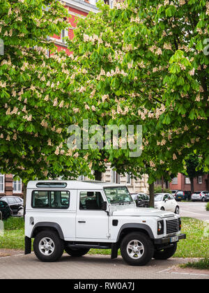 STRASBOURG, FRANCE - Le 6 mai. 2017 : Blanc porte trois land rover defender 4X4 garé en ville sous le châtaignier arbre en fleur Banque D'Images