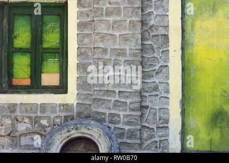 Fragment d'un mur de pierre d'une maison avec une fenêtre verte et une porte verte. Banque D'Images