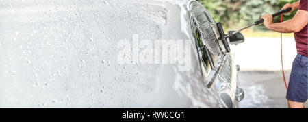 L'homme lave sa voiture au lave-auto libre service, nettoyage des pinceaux couverts en verre dans le shampooing. Le côté gauche est étendue à la taille de la bannière, de l'espace pour le texte. Banque D'Images