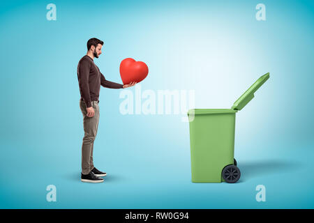 Man throwing red heart en poubelle ouvert sur fond bleu Banque D'Images