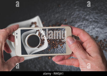 Man taking photo de tasse de café blanc et les grains de café sur la table en pierre noire Vue de dessus Banque D'Images