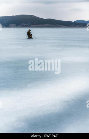 Pêcheur sur glace hiver gelé lac de montagne en Bulgarie Batak pendant les derniers jours de l'hiver 02.03.2019 Banque D'Images