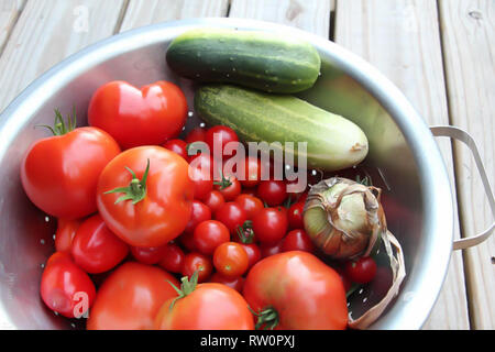 Libre bol en métal plein de tomates et concombres fraîchement cueillies sur terrasse en bois Banque D'Images