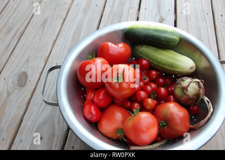 Bol en métal plein de tomates et concombres fraîchement cueillies sur terrasse en bois Banque D'Images