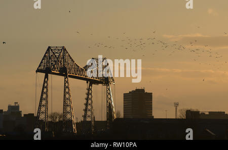 Pont du transporteur de Middlesborough éclairé par un soleil en fin d'après-midi avec un troupeau d'oiseaux qui volent à côté Banque D'Images