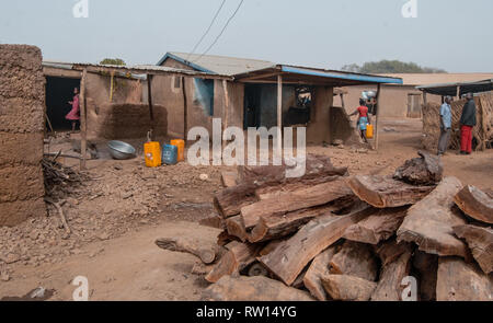 Une belle photo de petites maisons et des personnes à une petite rue naturelles en milieu rural au Ghana. Pile de bois de chauffage est vu sur l'avant-plan. Banque D'Images