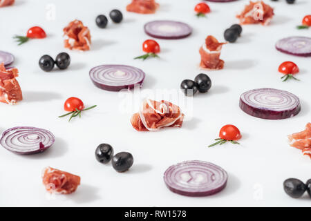 Focus sélectif des oignons rouges près de prosciutto et de tomates cerise avec des brindilles de romarin sur fond blanc Banque D'Images