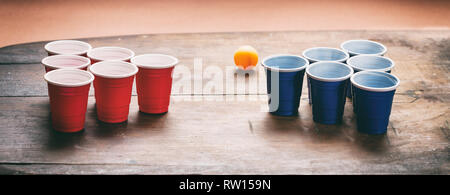 Beer Pong, college party game. Couleur bleu et rouge en plastique tasses et balle de ping-pong sur fond de bois, la bannière Banque D'Images