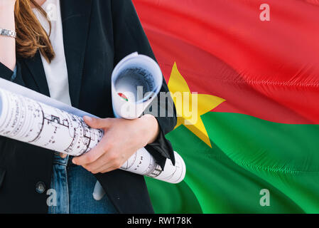 Femme architecte holding blueprint contre le Burkina Faso waving flag background. Construction et architecture concept. Banque D'Images