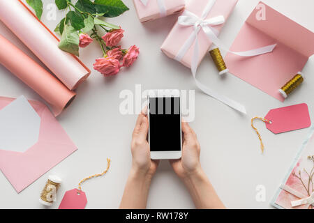 Portrait of woman holding smartphone près de roses, rouleaux de papier, les cadeaux emballés, enveloppe, carte et des bobines de fil sur fond gris Banque D'Images