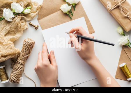 Portrait de femme écrit dans un stylo à encre avec carte près de fleurs, tissu, et enveloppe cadeau enveloppé sur fond gris Banque D'Images