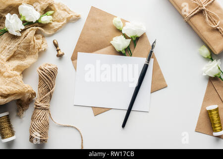 Vue du dessus de l'enveloppe avec un stylo à encre et carte vide, fleurs, tissu, stamp, cadeau enveloppé sur fond gris Banque D'Images