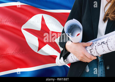 Architecte nord-coréen woman holding blueprint contre la Corée du Nord waving flag background. Construction et architecture concept. Banque D'Images