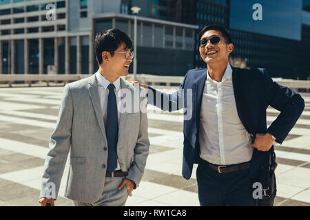 Deux smiling asian businessmen talking et marcher dans la ville. Partenaires d'affaires à marcher ensemble à l'extérieur. Banque D'Images